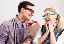 Two cute young adults laughing and holding flowers