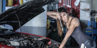 A dirty woman working under the hood of a car