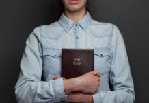 Woman holding a Bible in hands over the gray background