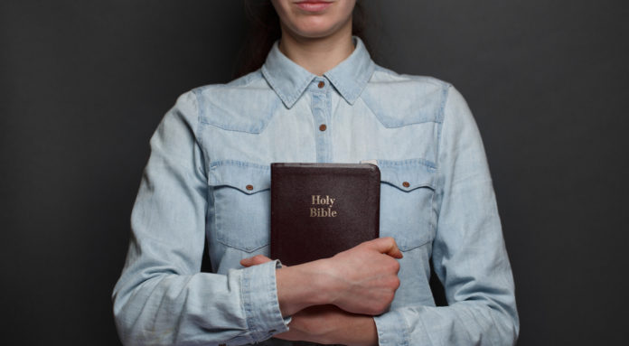 Woman holding a Bible in hands over the gray background