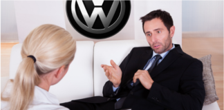 Man laying on couch while psychiatrist woman writes diagnosis. Volkswagen logo on wall