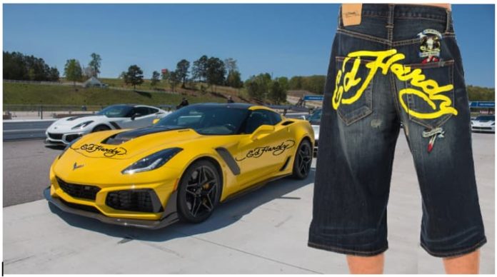 Man wearing baggy jean shorts with Ed Hardy across the rear, yellow 2019 Chevrolet Corvette with Ed Hardy text in back