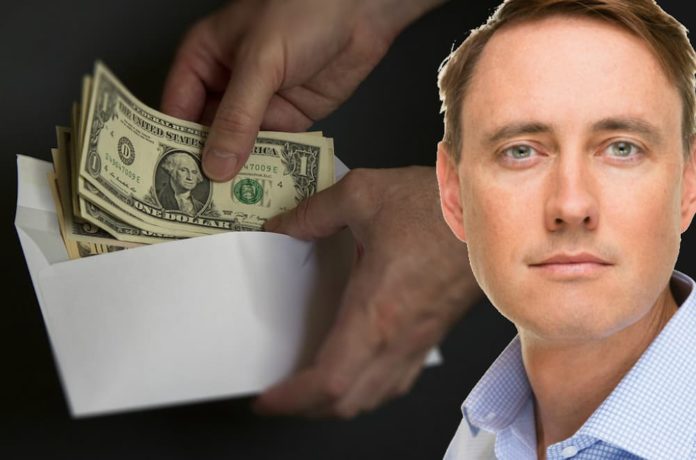 A man's face is shown over a black background with hands holding an evelope of dollar bills behind him. The man was debating the 2019 Chevy Silverado vs 2019 Ram 1500.