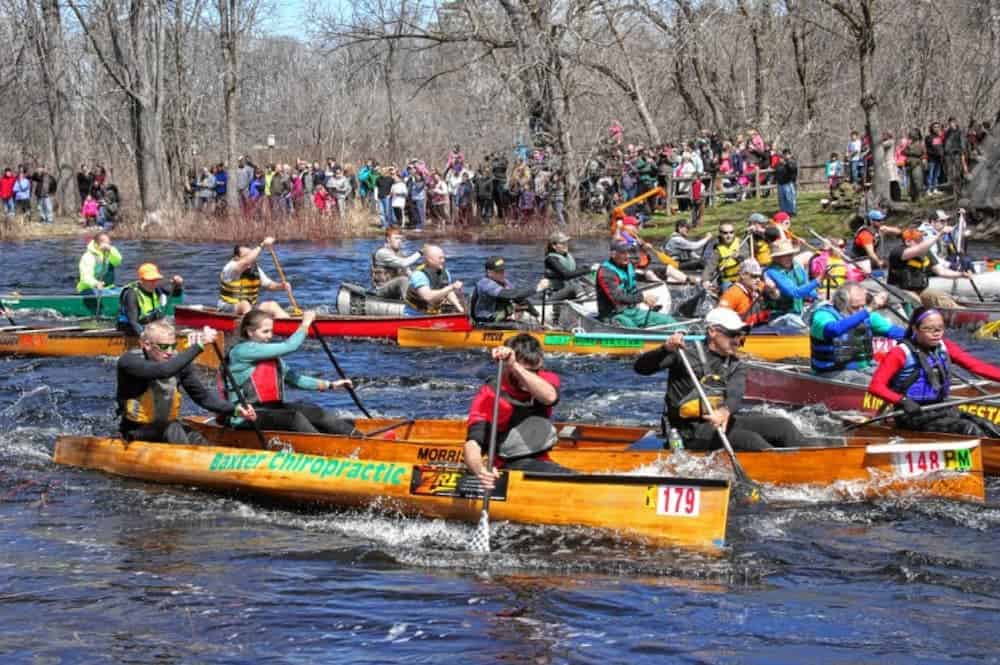 Many colorful canoes are racing in the river with people watch from the banks.