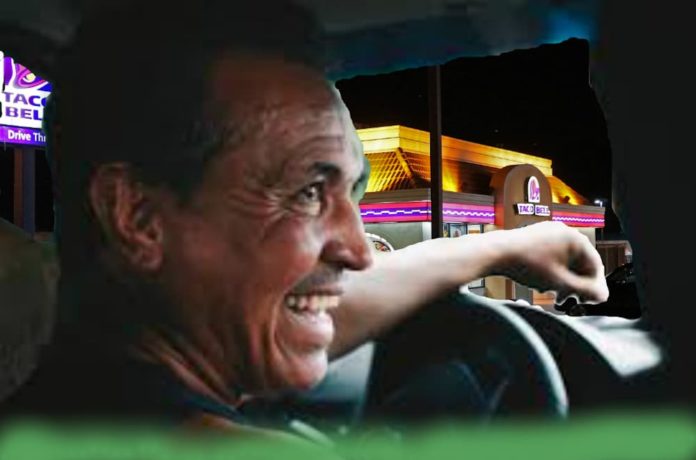 A sweaty laughing man is driving past a Taco bell.