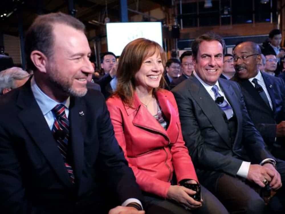 Three GM executives are sitting in a crowd and smiling.