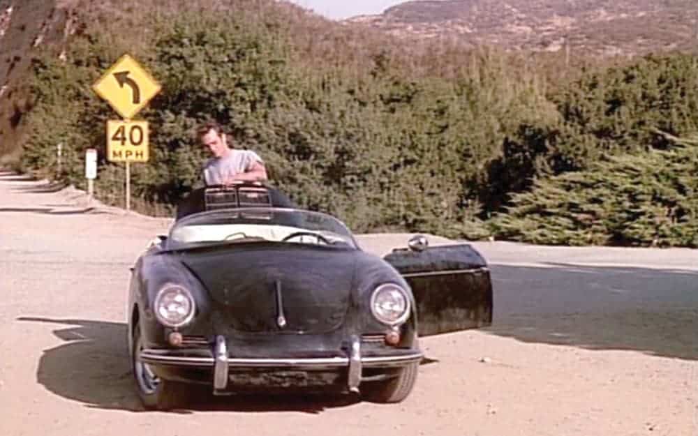 Luke Perry is shown standing behind the black convertible Porsche speedster from '90210' on a road pull off.