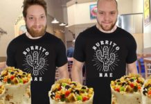 Two men in Burrito Bae shirts are in a restaurant with burritos in front of them.