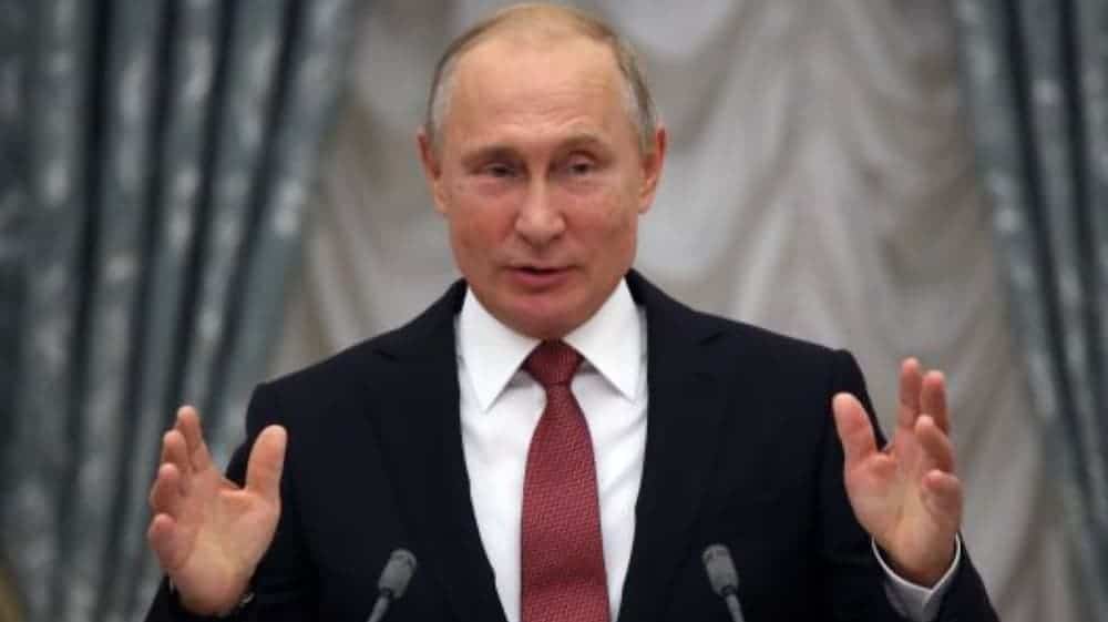 Vladamir Putin is giving a speech with his hands up in front of him.