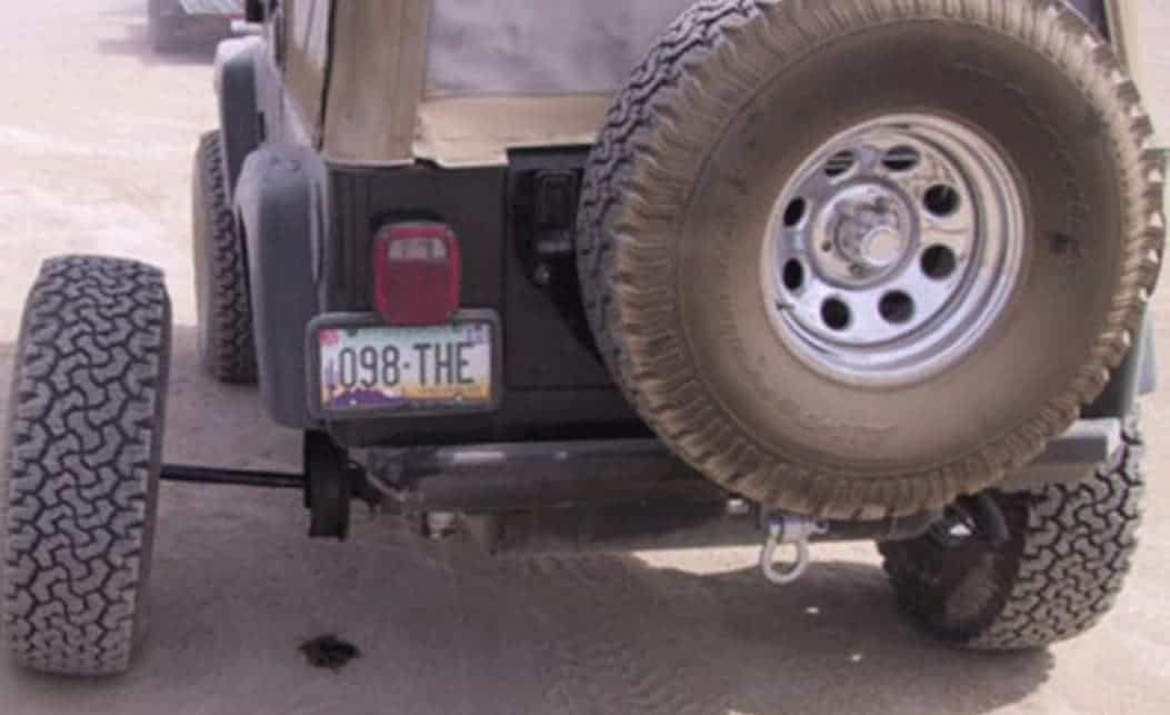 A Jeep Wrangler has a broken axle with the tire and shaft falling off.