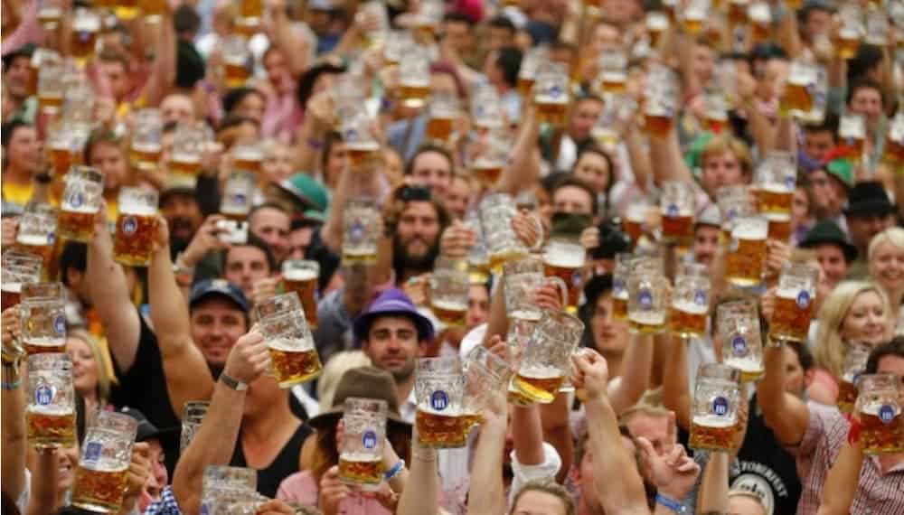 A crowd holding up beer mugs is shown.