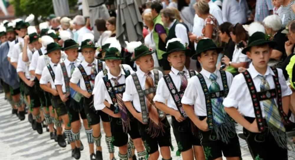 A line of German kids are dressed in traditional outfits.