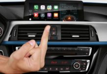 A hand is flipping off the BMW Apple CarPlay feature which is a topic in live auto news.