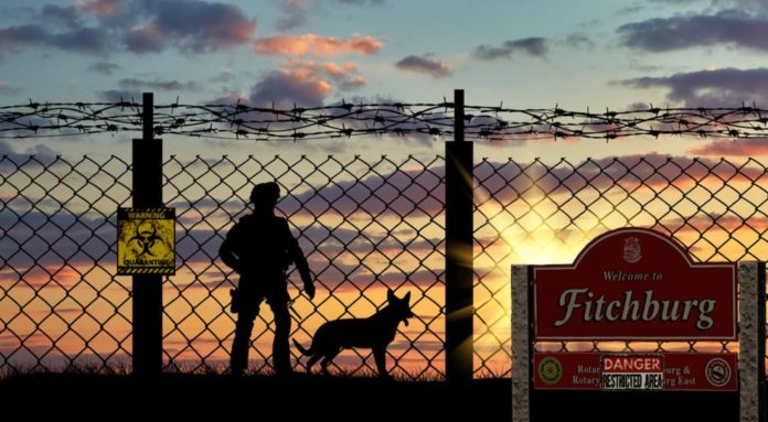 A National Guard soldier is standing behind a fence with the 'Welcome to Fitchburg' sign in front of it after fights break out between 2019 Ford Fusion vs 2019 Kia Optima.