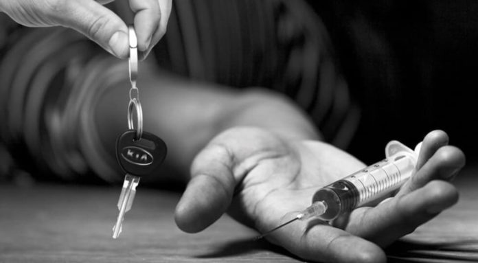 A close up is shown of a hand holding a syringe with a Kia car key next to it.