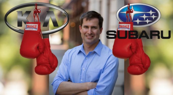 The Kia and Subaru logos have boxing gloves hanging off of them, while Congressman Seth Moulton is in the middle smiling.