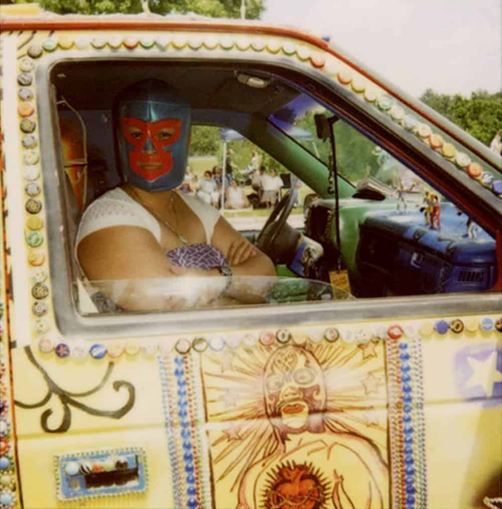 A woman with a Mexican wrestling mask is in a artistically painted car.