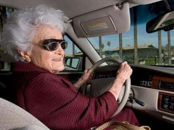 An old lady is driving a used Cadillac with an eye cover over her eyes.