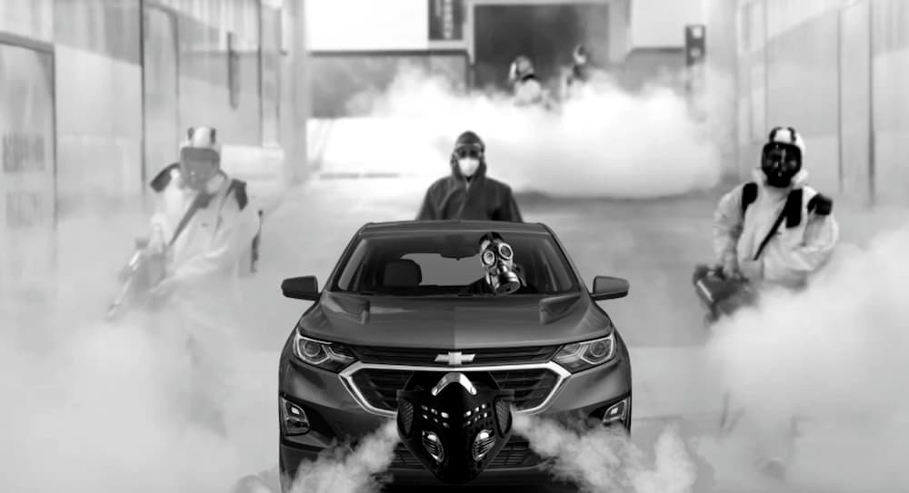 Masked workers surround a masked Chevy car, shown in black and white.