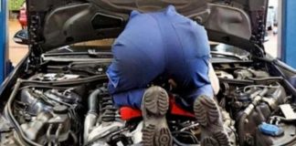 A mechanic is bent over under the hood of a car for a scheduled service.