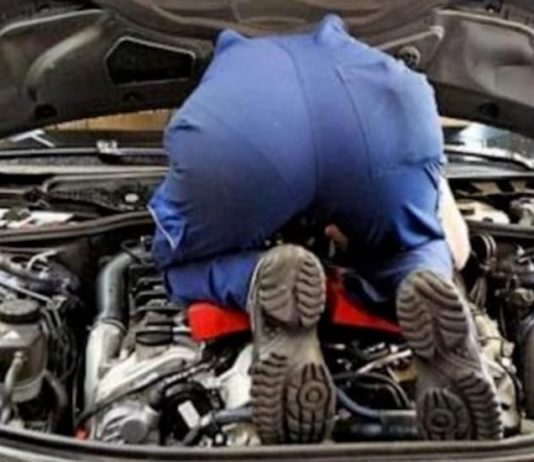 A mechanic is bent over under the hood of a car for a scheduled service.