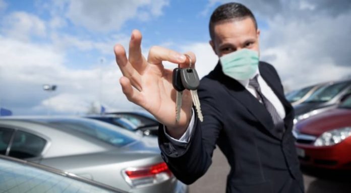 A salesman with a medical mask is holding keys in front of used cars in Columbus, Ohio.