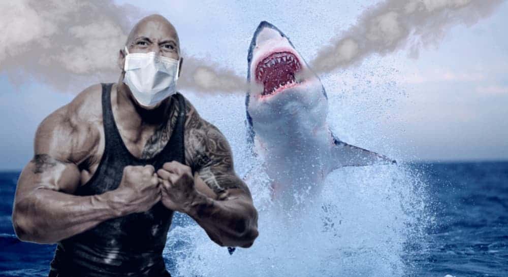 The Rock has a mask on as a shark jumps from the water behind him.