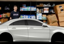 A man is standing behind a white car with his boxes of cleaning supplies.