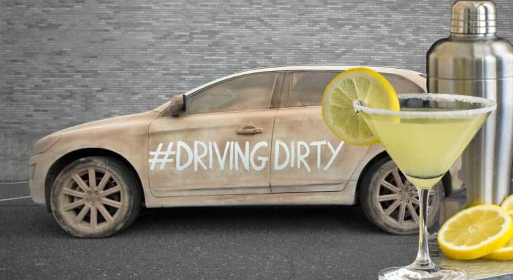 A martini is in front of a dirty car that has #drivingdirty written on it, which is not advised when you want to sell your car.