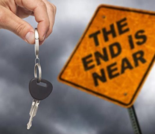 A hand is holding keys in front of a sign that says 'The End is Near.'