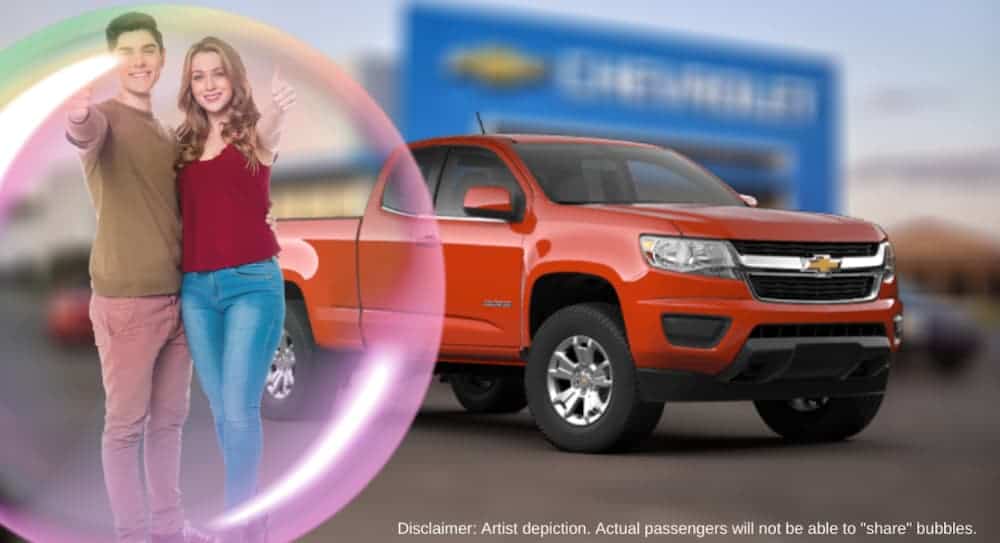 A couple is in a bubble in front of a red 2020 Chevy Colorado at a dealership.