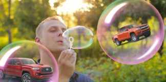 A man is blowing bubbles with two red trucks, the 2020 Chevy Colorado vs 2020 Toyota Tacoma, in them.