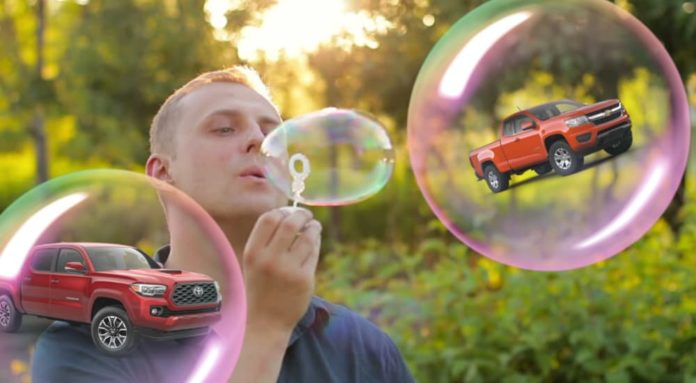 A man is blowing bubbles with two red trucks, the 2020 Chevy Colorado vs 2020 Toyota Tacoma, in them.