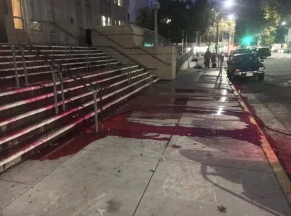 Blood is running down stairs and the sidewalk on a city street.