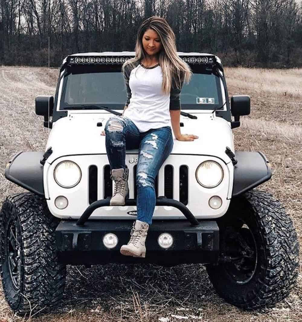 A 'Jeep girl' is sitting on the hood of her modified white Jeep Wrangler.