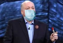 Ford CEO Jim Hackett is shown giving a speech while wearing a mask and with a virus pin.