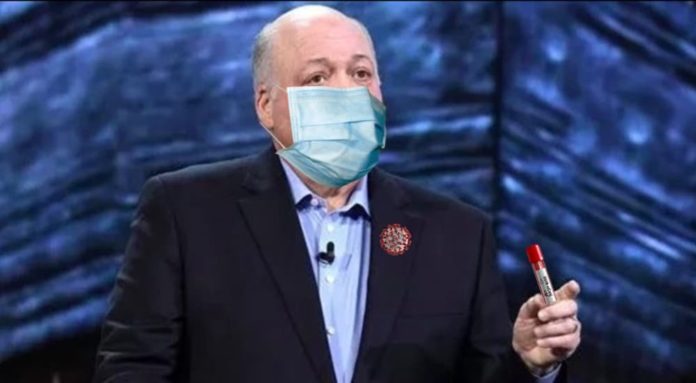 Ford CEO Jim Hackett is shown giving a speech while wearing a mask and with a virus pin.