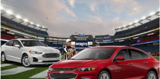 A white 2020 Ford Fusion, a red 2020 Chevy Malibu and a referee are on the field of a football stadium.