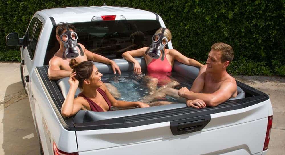 Four friends are in a truck bed pool, two with gas masks on, discussing the differences between the 2020 Jeep Gladiator vs 2020 Chevy Colorado.