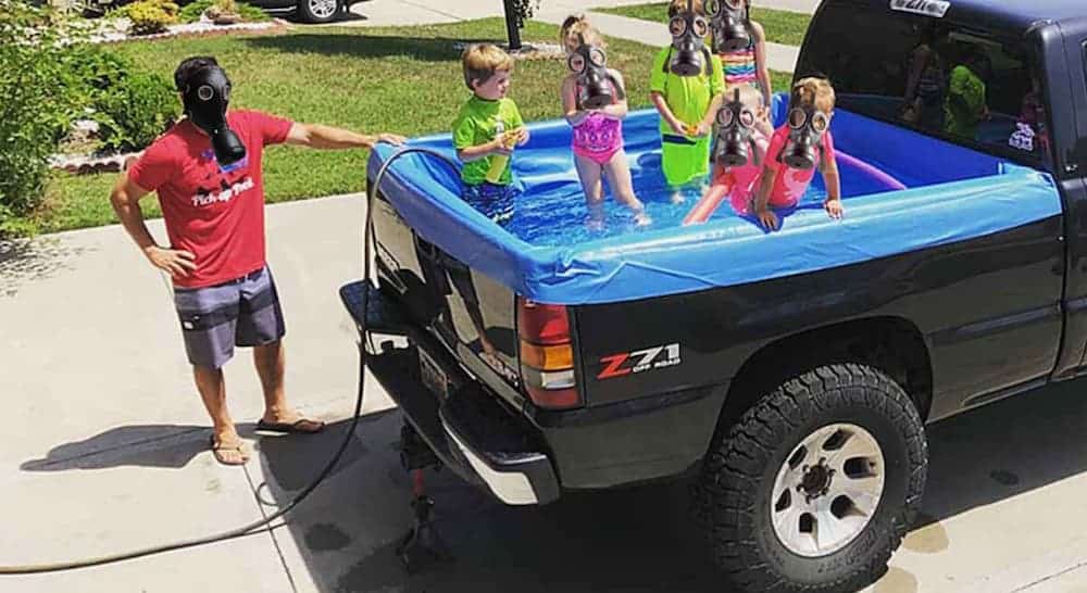 A man is filling up his truck bed pool with kids playing in it.
