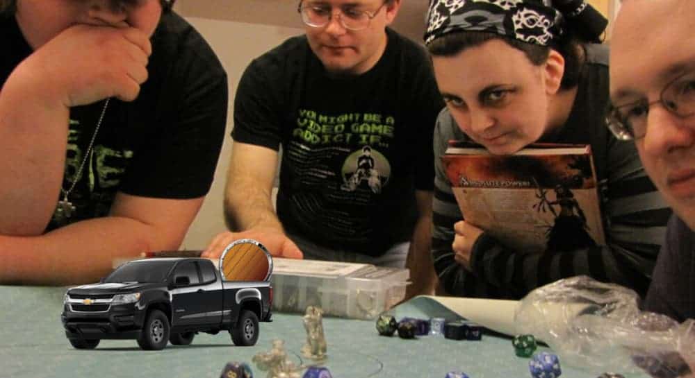 Awkward teens are around a table with a D&D game and a mini Chevy truck on it.