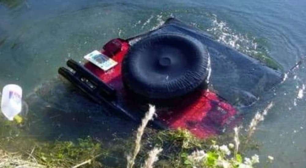 A red Jeep model Wrangler is shown face down submerged in water.