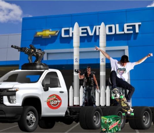 A skateboarder is doing a trick in front of a used Chevy truck fitted with rockets and gun turrets next to a box of mountain dew and a Terminator, in front of a Chevy dealership.