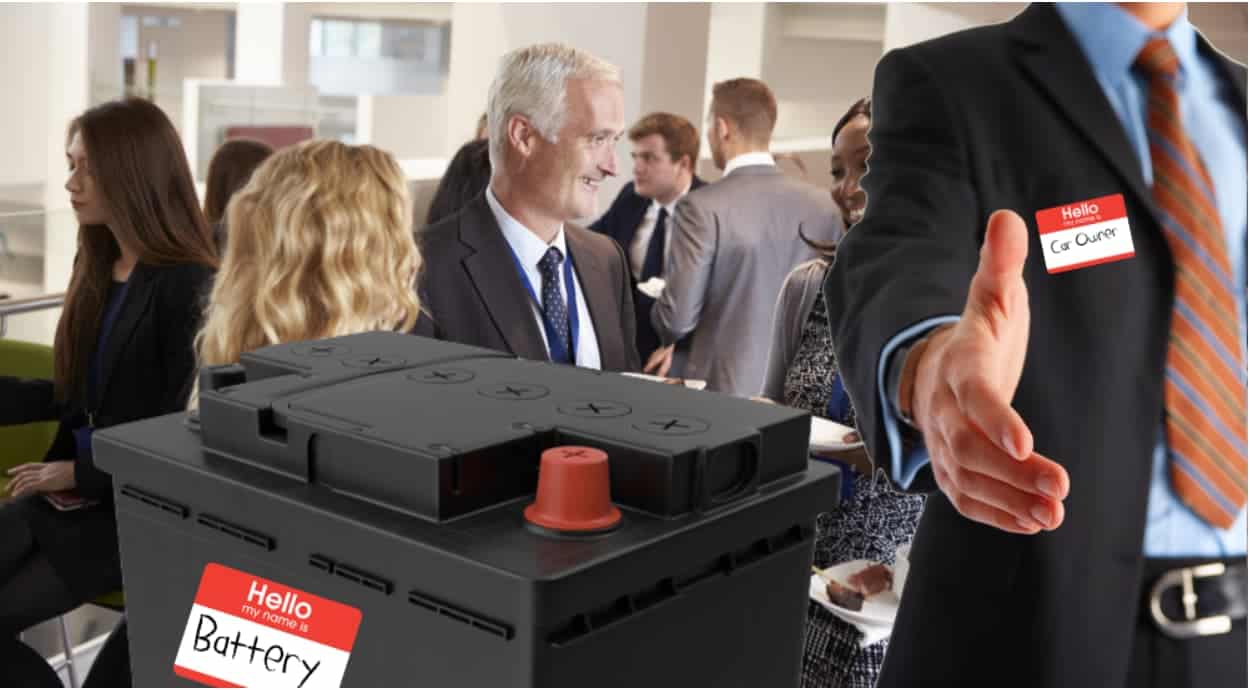 A car battery with a nametag is next to a man with his hand outstretched for a handshake.
