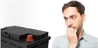 A man is biting his nails while staring at a car battery, an important step in car maintenance.