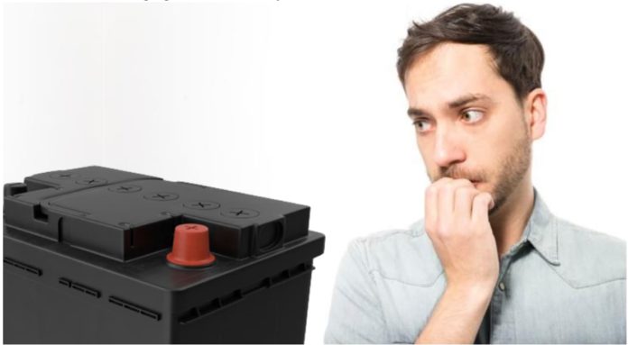 A man is biting his nails while staring at a car battery, an important step in car maintenance.
