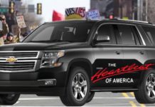 A black 2021 Chevy Tahoe with the words 'the hearbeat of America' on the side is parked in front of a protest.
