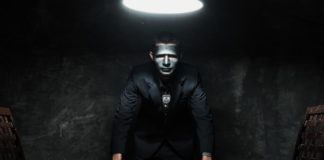 A man with a black mask and Ram logo is looking over a table in a dark room.