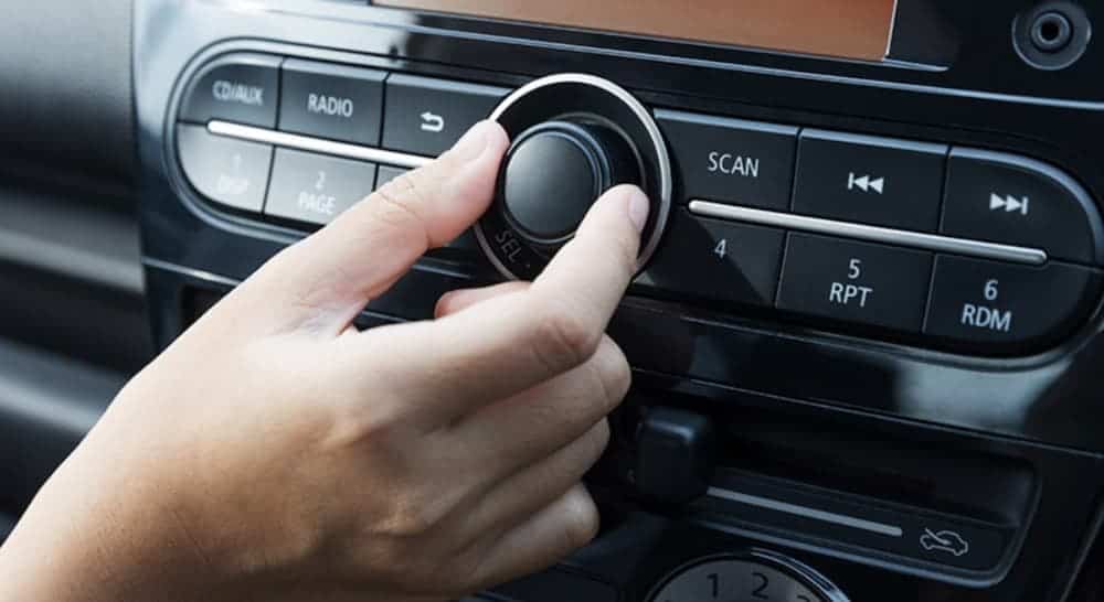 A closeup shows a hand adjusting the car radio volume.