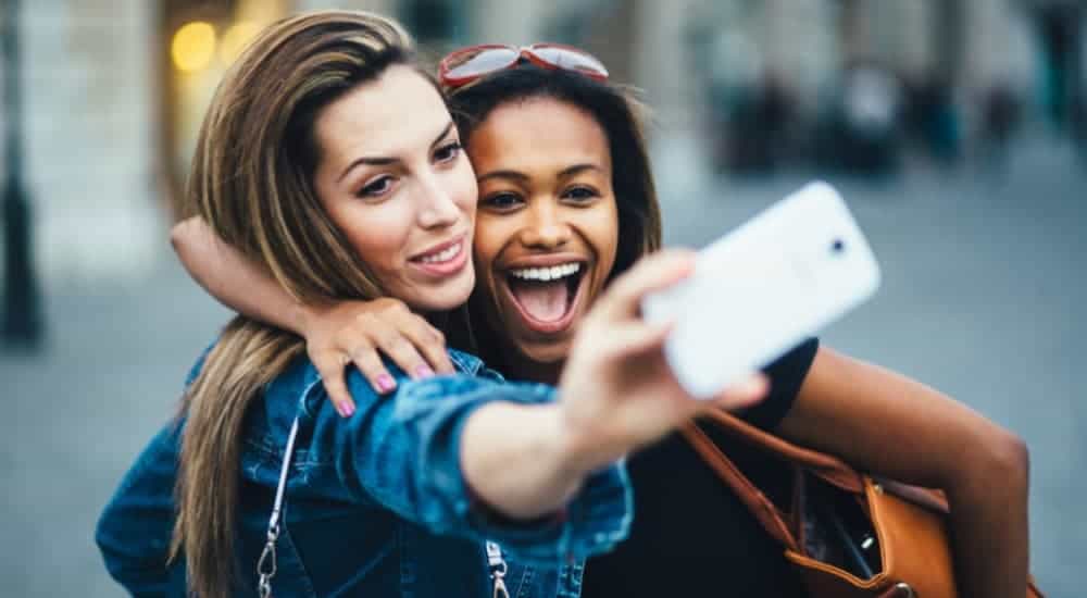 Two woman are embracing while holding up a cell phone to take a selfie.